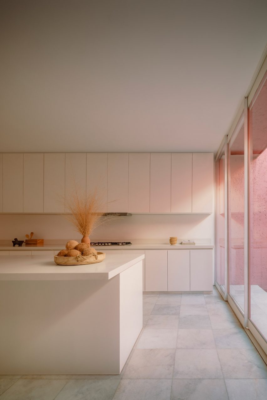 Белая кухня с минимально детализированными шкафами и розовым светом, проникающим справа