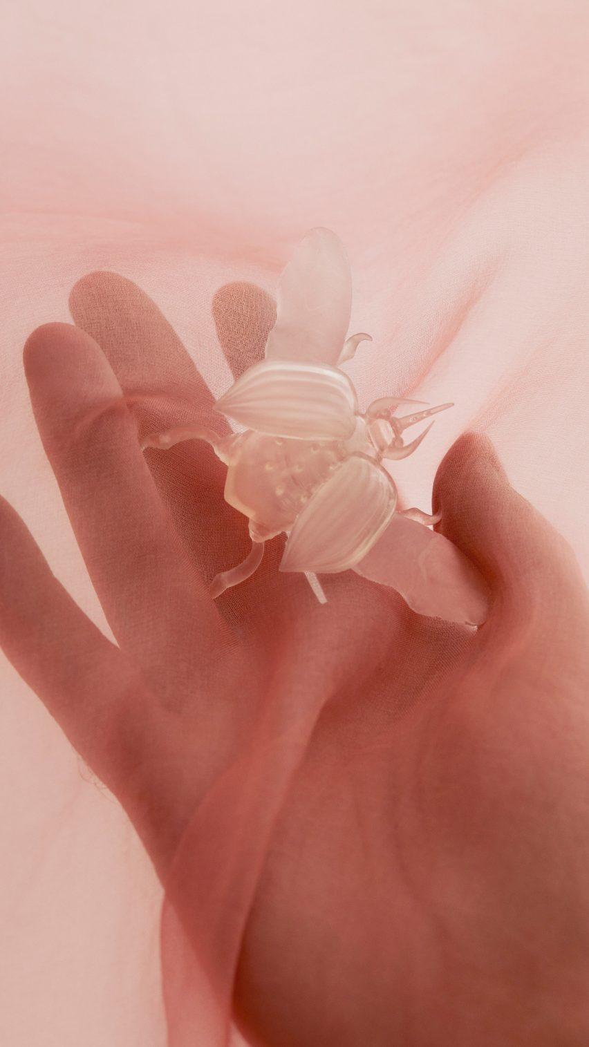 Рука держит полупрозрачного жука, напечатанного на 3D-принтере