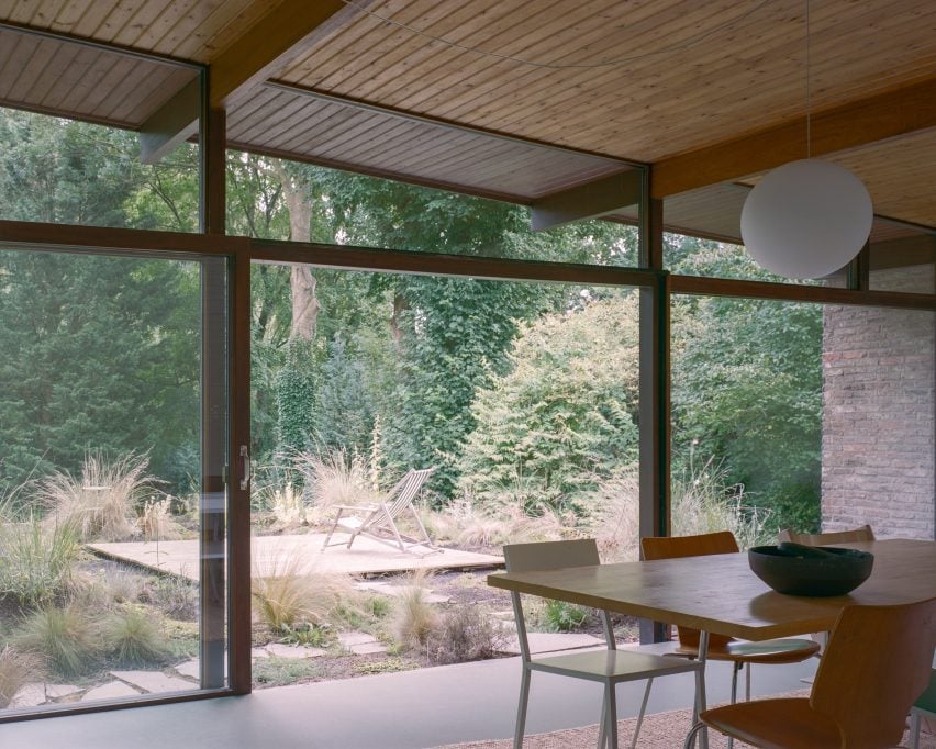 Столовая открытой планировки с застекленным фасадом с деревянным каркасом и видом на сад.