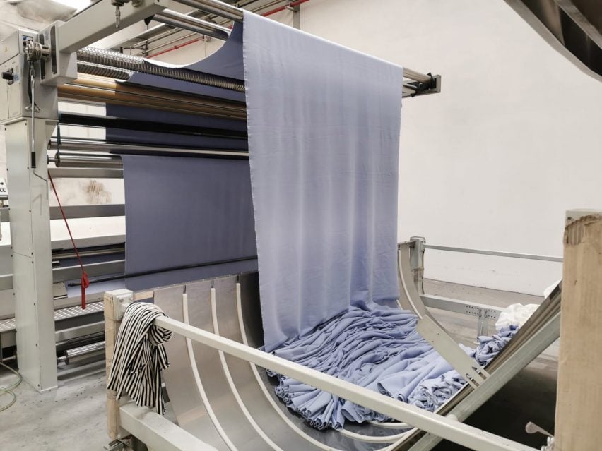 Фотография бледно-голубой ткани, протягиваемой через промышленные машины.