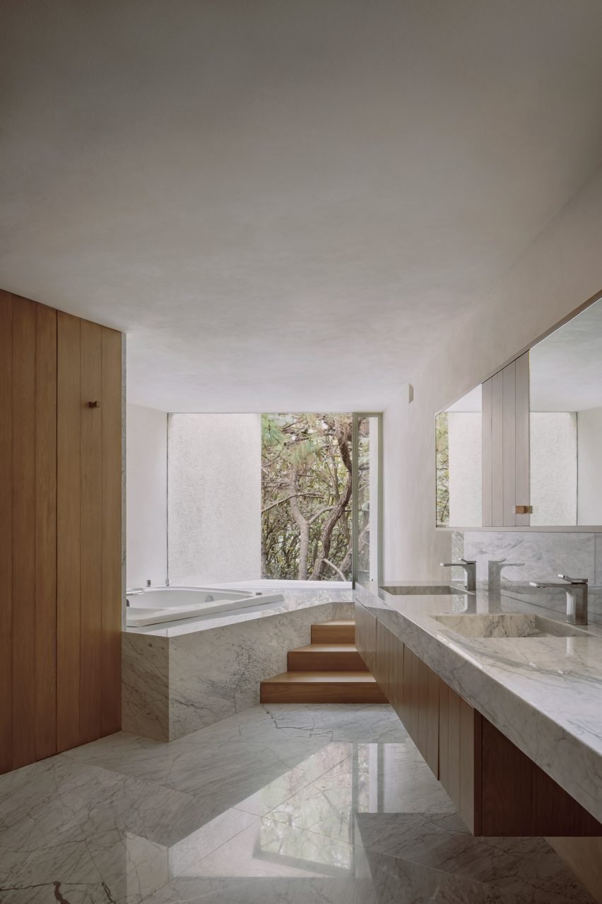 Ванная комната с мраморными поверхностями и окном с видом на лес.