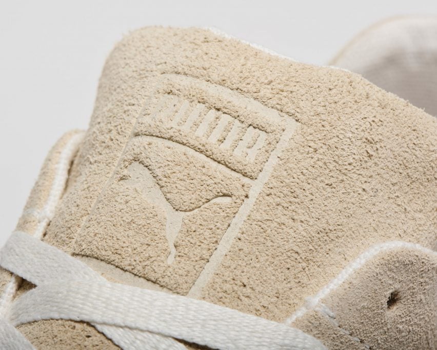 Крупный план язычка кроссовок Puma Re:Suede: верх из замши кремового цвета с тисненым логотипом Puma и белоснежными конопляными шнурками.