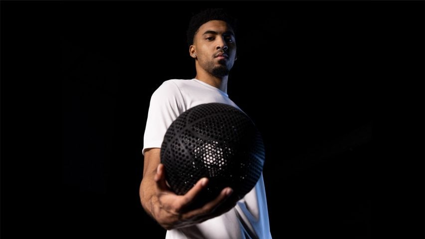 Мужчина в белой футболке держит черный безвоздушный баскетбольный мяч, распечатанный на 3D-принтере Wilson.