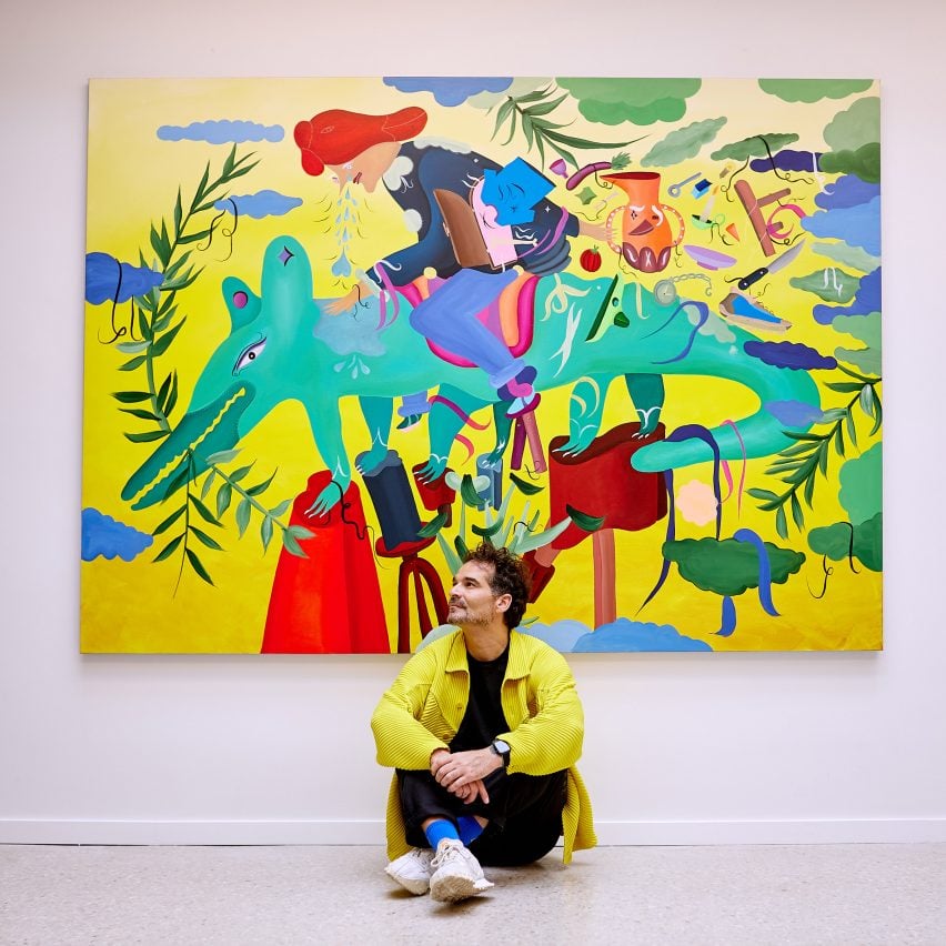Джейми Хэйон сидит перед картиной, на которой изображен человек верхом на зеленом существе.