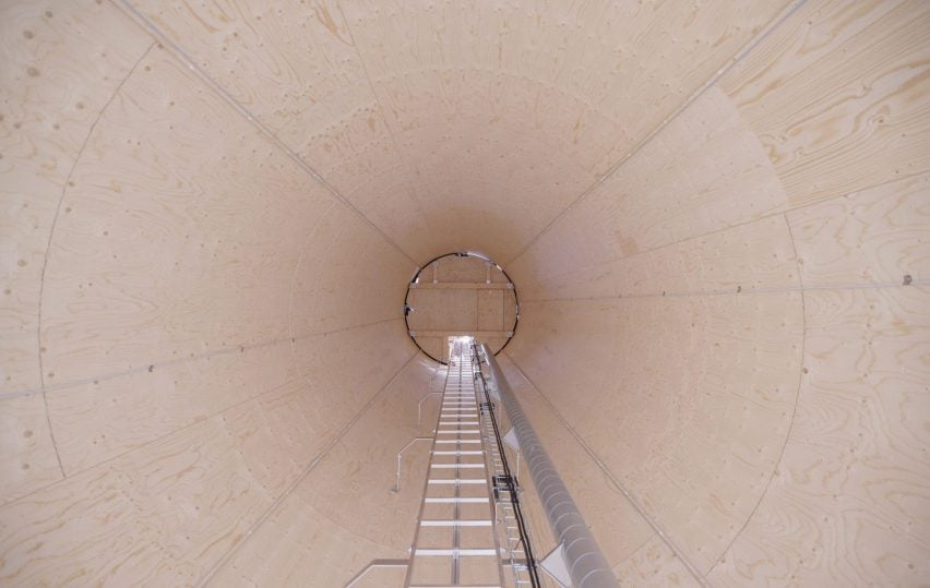 Фотография внутренней части большого деревянного цилиндра с лестницей, идущей посередине.