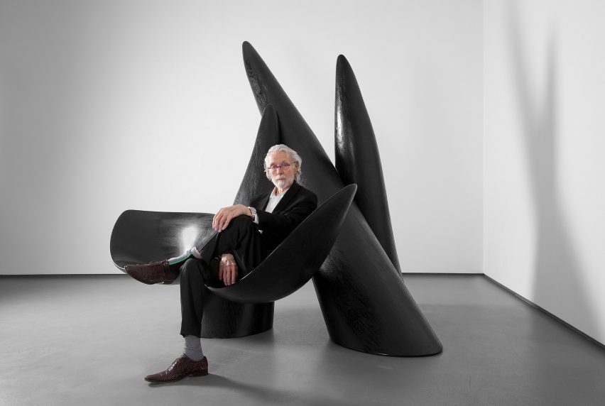 Фотография Касла Венделла в последние годы его жизни, сидящего на одной из своих больших черных биоморфных скульптур.