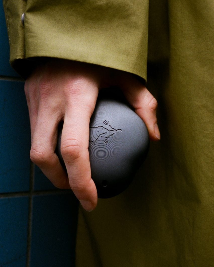 Фотография руки, сжимающей темно-серое похожее на камень устройство, украшенное фигурой идущего человека. 