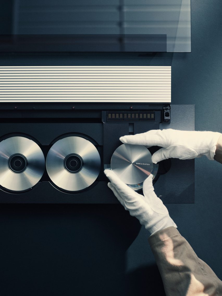 Фотография сверху: руки в белых перчатках держат компоненты проигрывателя компакт-дисков Beosound 9000 во время его чистки и восстановления.