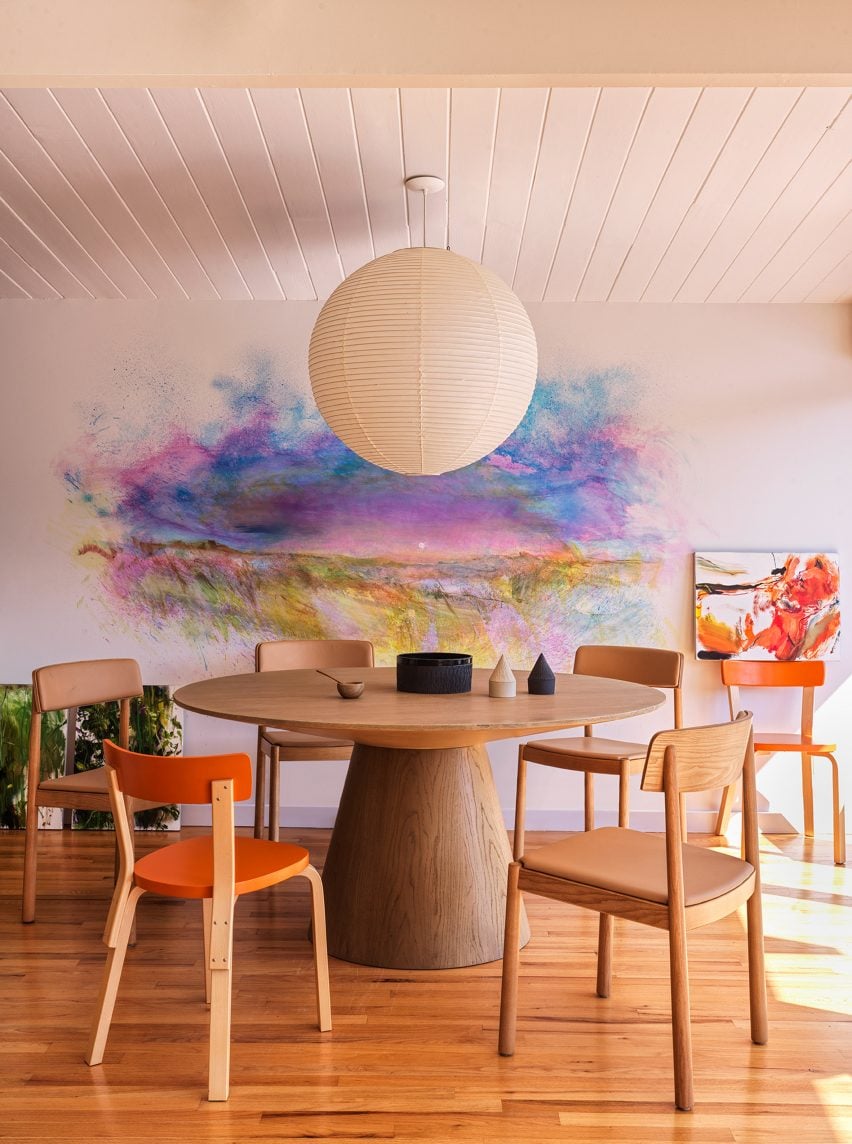 Обеденный стол со сферической подвесной лампой и яркими картинами.